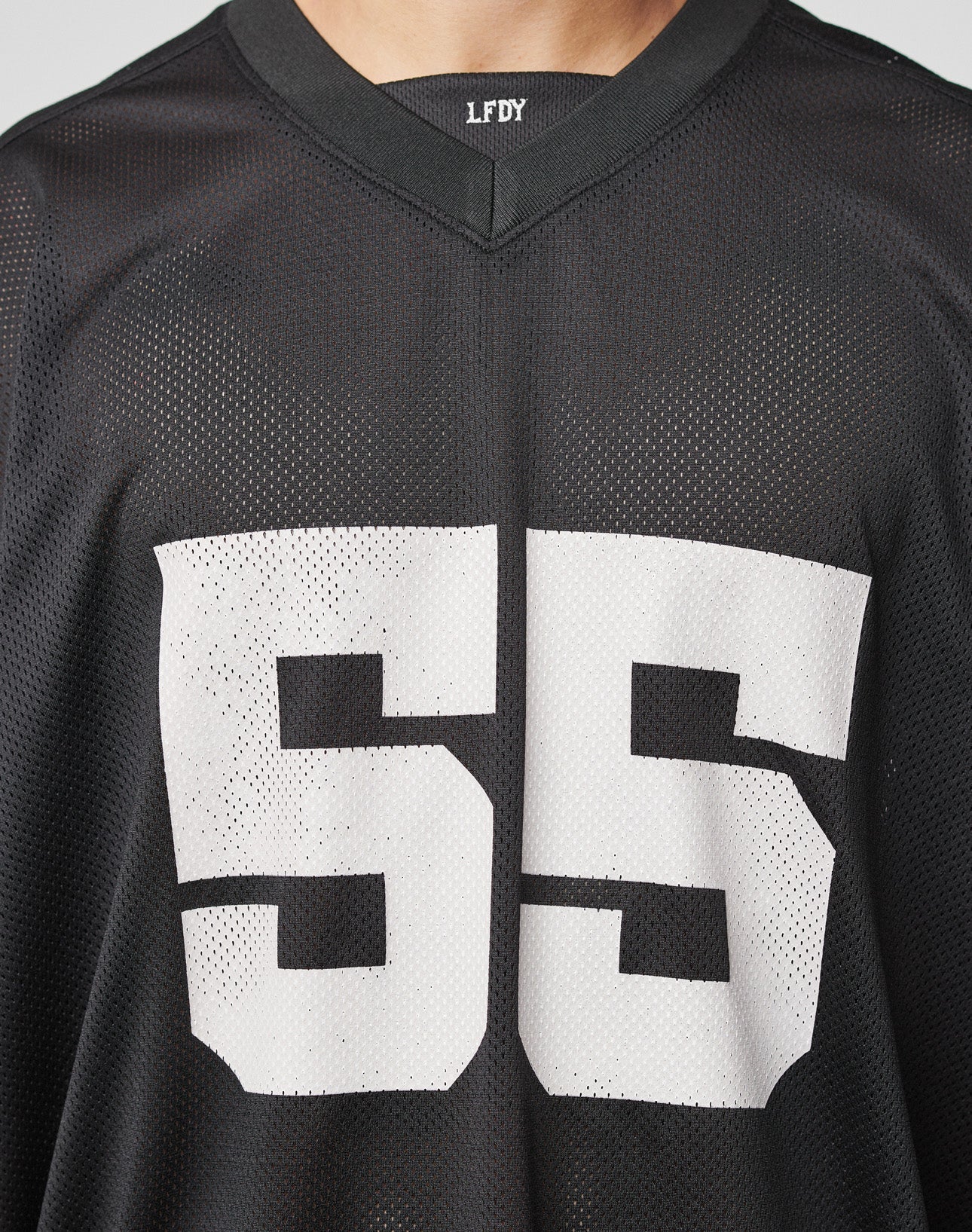 A person wearing the LFDY Mesh Jersey by LIVE FAST DIE YOUNG, featuring an oversized black mesh design, large white number 55 on the front, and LFDY lettering near the V-neck collar. Only the upper torso is shown.