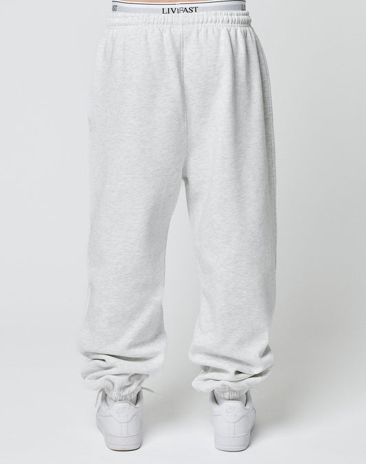 Model wears the LIVE FAST DIE YOUNG Basic Loose Jogger in light gray with Elastik-Bund and subtle logo, white LIVFAST waistband showing, paired with white sneakers, photographed from behind against a plain background.