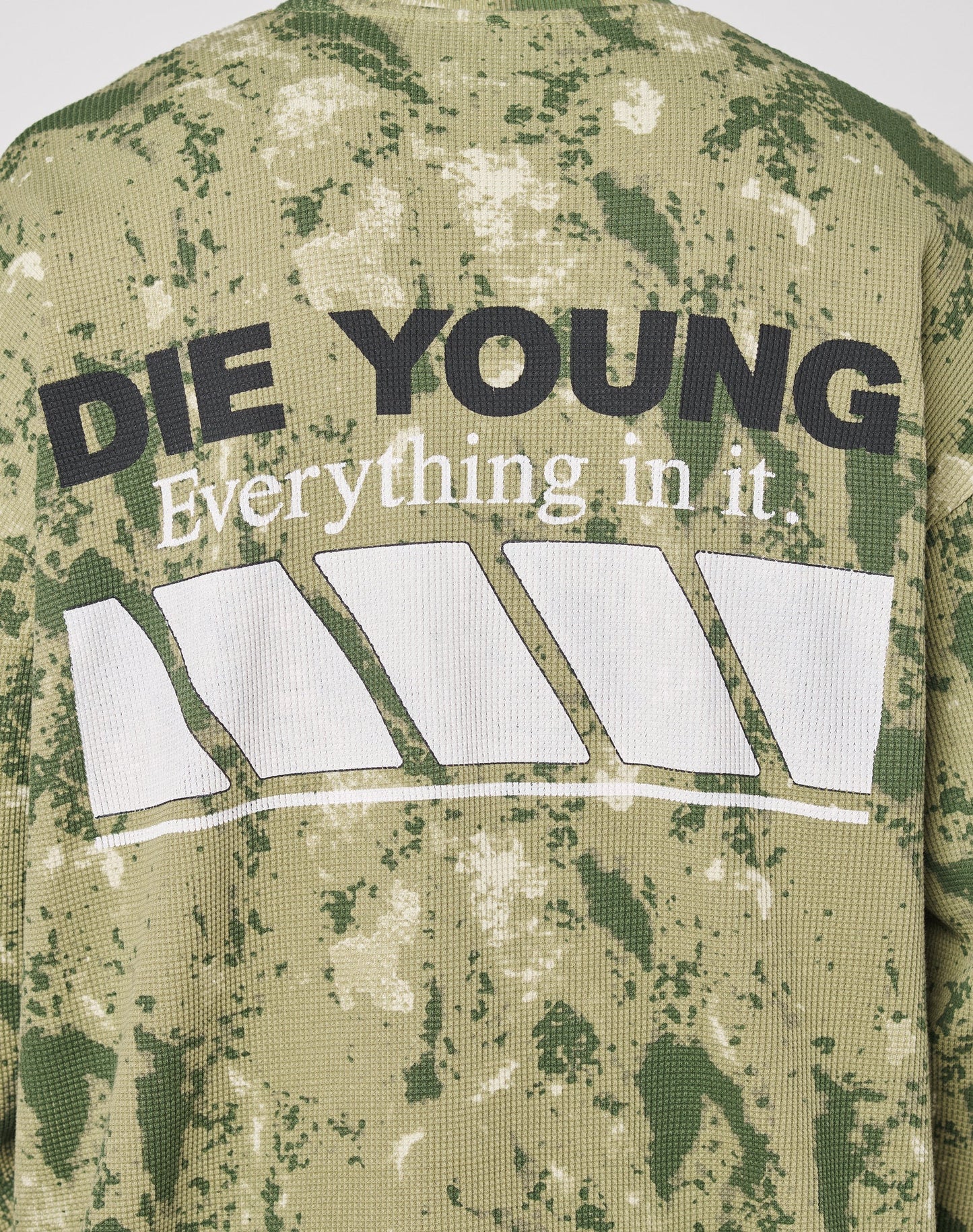 The LFDY Racing Waffle Longsleeve by LIVE FAST DIE YOUNG features a green and beige camo print, bold black DIE YOUNG front text, white lettering below, a geometric graphic, and an oversized fit in 100% cotton.