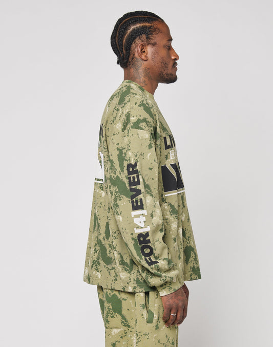A man with braided hair is in profile, wearing the LFDY Racing Waffle Longsleeve by LIVE FAST DIE YOUNG, featuring an oversize green and beige camo pattern, 100% Baumwolle, with FOR 4EVER in white on the sleeve and matching pants.