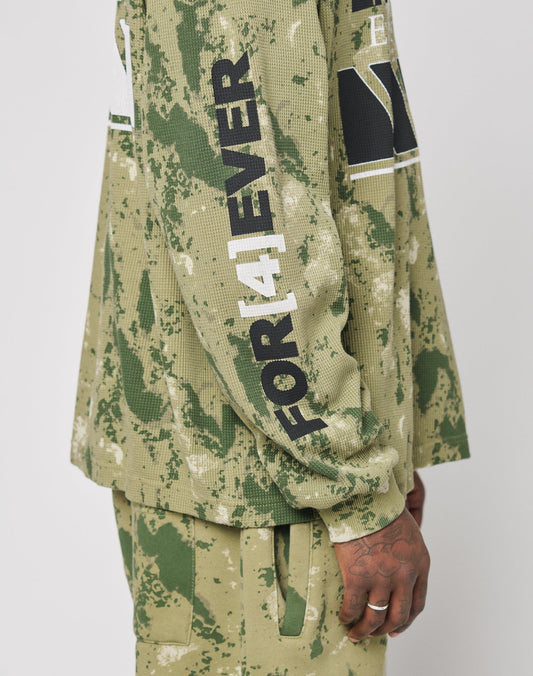 A person wears the LFDY Racing Waffle Longsleeve by LIVE FAST DIE YOUNG—an oversize, green camouflage Baumwolle top with FOREVER in black and white on the sleeve. Their hand rests at their side against a plain background.