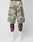 Someone is seen from the back wearing LIVE FAST DIE YOUNG Army Shorts in green camouflage with cargo pockets, styled with white socks and sneakers against a plain light background for a casual vintage vibe.