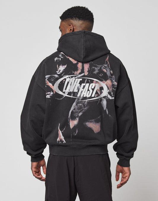 A person wearing the LFDY Canine Hooded Zip by LIVE FAST DIE YOUNG, featuring a bold snarling dogs graphic and “LIVE FAST” in silberner Druck on the back, stands with their back to the camera.