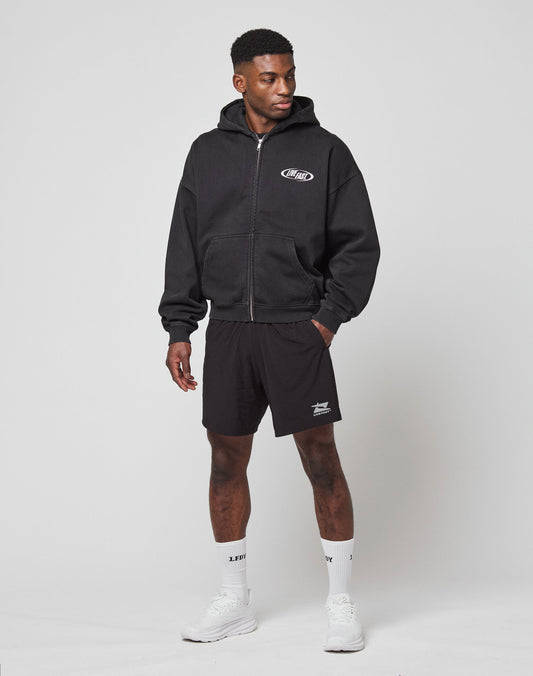 A man stands against a plain background wearing the LFDY Canine Hooded Zip by LIVE FAST DIE YOUNG, black shorts, white crew socks, and white sneakers. He has one hand in his pocket and looks to the side.