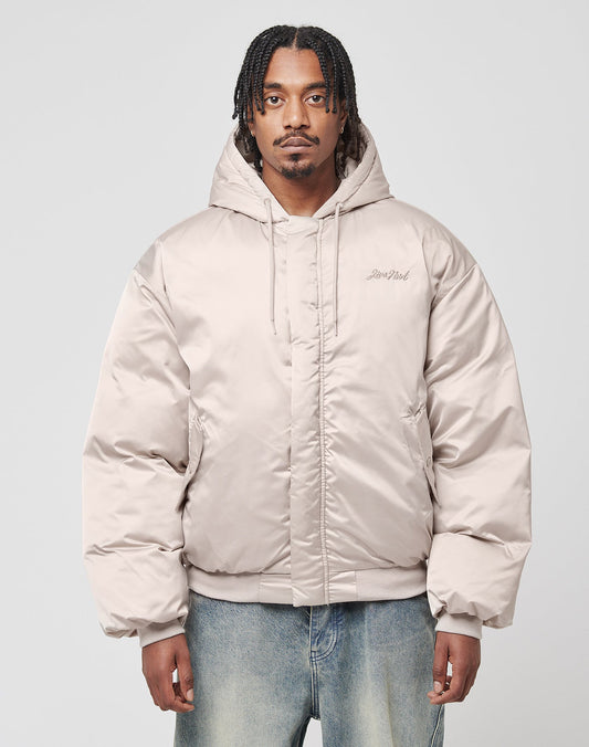 A man with braided hair wears the LFDY Winter Bomber Jacket by LIVE FAST DIE YOUNG in light beige with Kapuze and Oversize Fit, paired with loose-fitting jeans, standing against a plain light gray background.