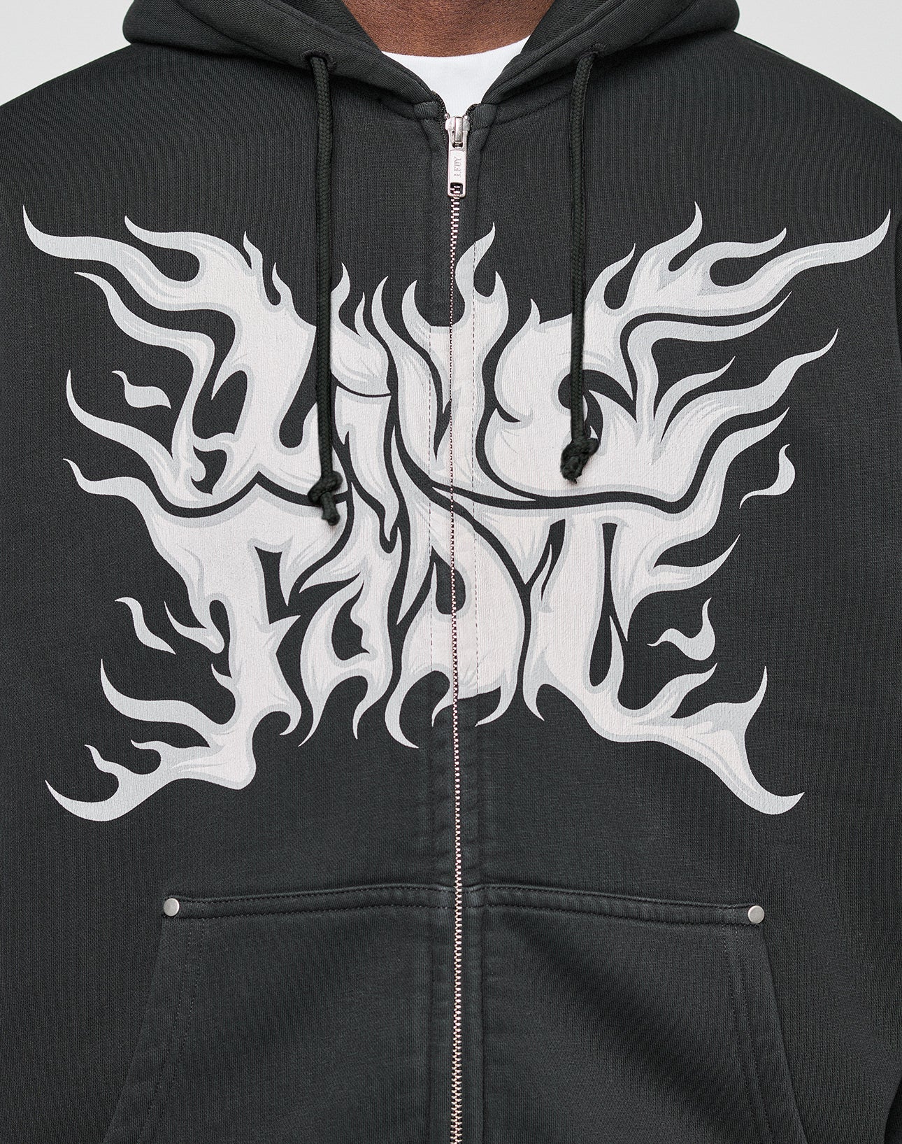 Someone wears the LFDY Inferno Hooded Zip by LIVE FAST DIE YOUNG, featuring an oversize fit, black individuelle Wascheffekt, zipper and drawstrings, plus bold Live Fast flame-like prints in white on the front and sleeves.