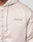 Close-up of a person wearing the LFDY Winter Bomber Jacket by LIVE FAST DIE YOUNG, a light beige oversized jacket with drawstring hood (Kapuze) and Live Fast cursive embroidery on the left chest. Partially visible zipper adds detail.