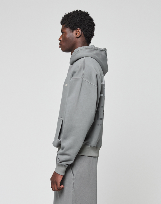 A person stands in profile against a light background, wearing the LIVE FAST DIE YOUNG Basic Evidence Hooded in gray with matching pants. The hoodie features a loose, oversized fit and a faded look, with hands resting by their sides.