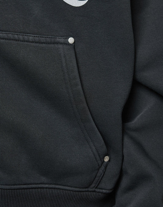 Close-up of the black LFDY Inferno Hooded Zip by LIVE FAST DIE YOUNG, showing its oversize pocket with visible stitching and three metallic rivets. The edge of a white front print hints at the individueller Wascheffekt on the fabric.