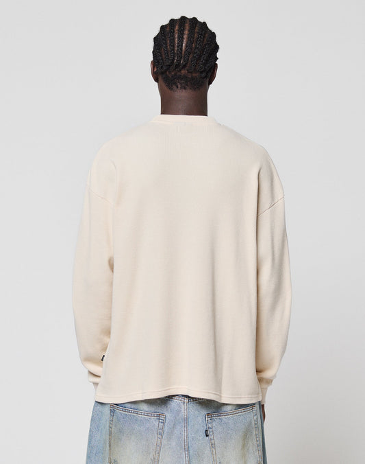 Seen from behind, a person with cornrow braids wears the LIVE FAST DIE YOUNG Blank Waffle Longsleeve—an oversize, cream 100% Baumwolle shirt—paired with light blue jeans, standing against a plain light background.