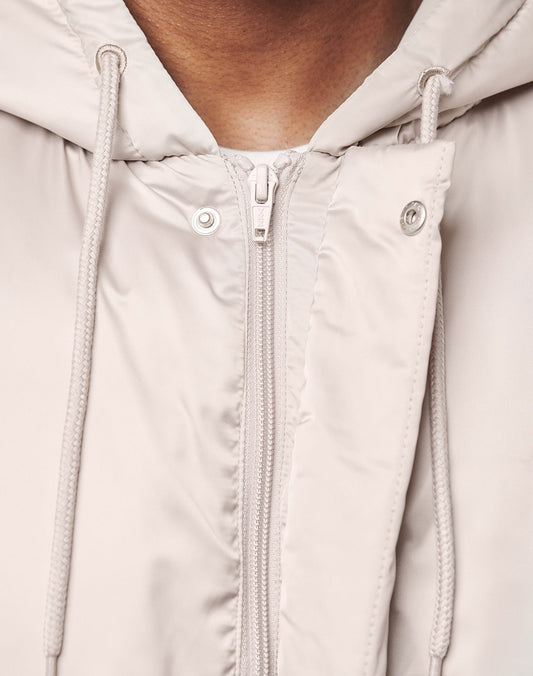 Close-up of a person wearing the LIVE FAST DIE YOUNG LFDY Winter Bomber Jacket in light beige with hood, showcasing zipper, snap buttons, and drawstrings. Its oversize fit and practical inner pocket offer comfort and functionality.