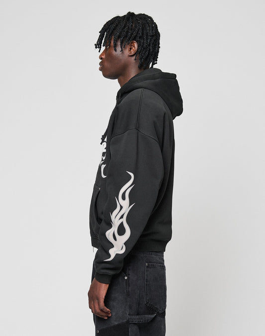 A person stands in profile against a plain background, wearing the LIVE FAST DIE YOUNG LFDY Inferno Hooded Zip with white flame print on the front and sleeves, paired with black jeans.