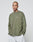 A person with a shaved head and tattoos wears the oversized LIVE FAST DIE YOUNG Basic Longsleeve in olive green (100% Baumwolle) and light gray pants, standing with hands in pockets against a plain light gray background.
