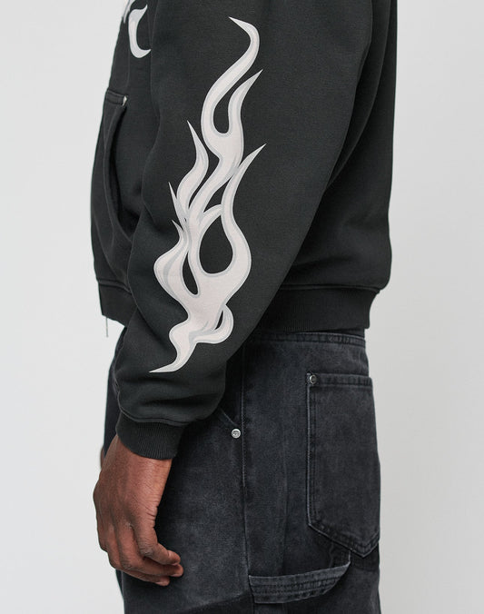 Someone wearing the LIVE FAST DIE YOUNG LFDY Inferno Hooded Zip with a bold white flame print on the front and sleeves, paired with dark denim jeans and shown in a side view.