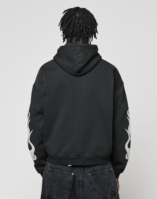 A person with short, twisted hair is facing away from the camera, wearing the LIVE FAST DIE YOUNG LFDY Inferno Hooded Zip with white flame front and sleeve print, paired with black jeans. The background is plain and light.