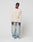 A person with braided hair and a neutral expression stands against a white background wearing LIVE FAST DIE YOUNG's Blank Waffle Longsleeve, oversize fit faded blue 100% Baumwolle jeans, and white sneakers.