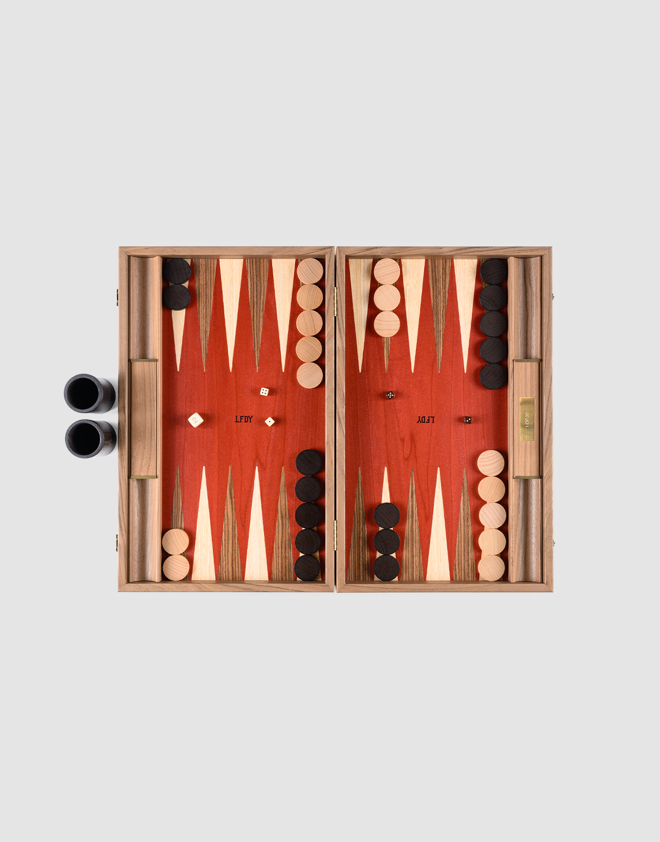 The LFDY Backgammon by LIVE FAST DIE YOUNG features a handcrafted board from Greece, black and white pieces set for play, two dice in the center, dice cups on the left, and a doubling cube on the right against a plain background.| plain 