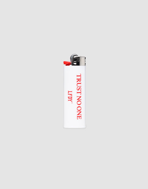 The LFDY Trust No One Lighter by LIVE FAST DIE YOUNG is a white BIC J26 with a chrome cap, red "TRUST NO ONE" on the front, "LEFTY" on the side, and delivers up to 3000 ignitions. Set against a plain light gray background.