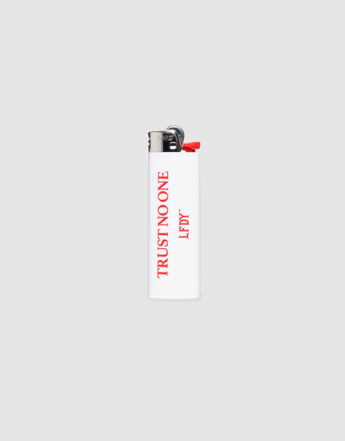 The LFDY Trust No One Lighter by LIVE FAST DIE YOUNG is a white BIC J26 with a chrome cap, red "TRUST NO ONE" and "LF DY" text, and offers up to 3000 ignitions. Photographed on a plain light gray background. 