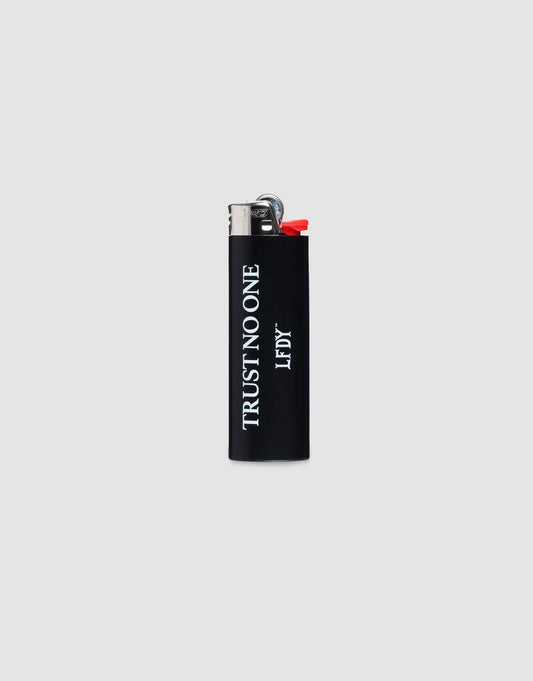 The LFDY Trust No One Lighter by LIVE FAST DIE YOUNG is a black BIC J26 with a chrome cap, TRUST NO ONE in white vertically, LF DY below, set on a plain light gray background. Bis zu 3000 Zündungen möglich.