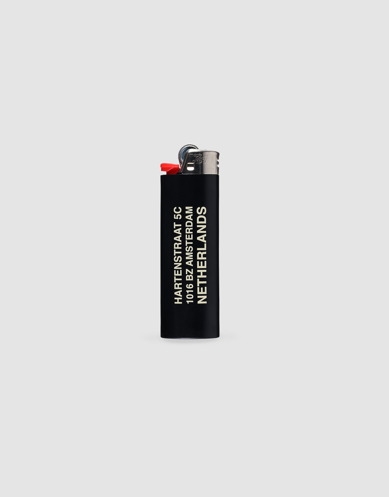 A black LFDY x The Bulldog Lighter by LIVE FAST DIE YOUNG with chrome cap and red ignition stands upright. “Hartenstraat 6, 1016 BE Amsterdam, Netherlands” is printed in white. Up to 3000 ignitions. Light gray background.
