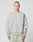 A person with short hair wears the LIVE FAST DIE YOUNG LFDY Wavy Sweater in light gray Oversize Fit, showcasing curved seam details and small white chest text, paired with light gray-green pants against a plain light background.