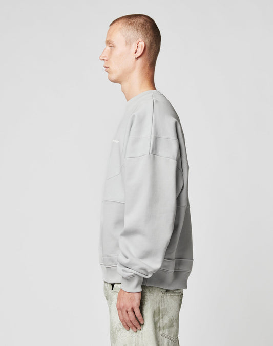 A man with short hair stands in profile, facing left, wearing the LIVE FAST DIE YOUNG LFDY Wavy Sweater and matching pants in light gray Oversize Fit cotton, against a plain white background.