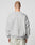 A person with a shaved head is seen from behind, wearing the LIVE FAST DIE YOUNG LFDY Wavy Sweater in light gray, featuring subtle curved stitching and an oversized fit, paired with textured light gray pants. The background is plain and light.