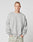 A young man with short hair wears the LIVE FAST DIE YOUNG LFDY Wavy Sweater, a loose light gray Baumwolle sweatshirt with curved stitching and chest text, paired with oversize light gray pants, standing against a plain white background.