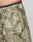 Close-up of a person wearing LIVE FAST DIE YOUNG Live Fast Nylon Shorts in green camo with oversized fit, black waistband with white text, side pockets, LIVE FAST Silikon-Print on the leg, and drawstring with plastic fastener.