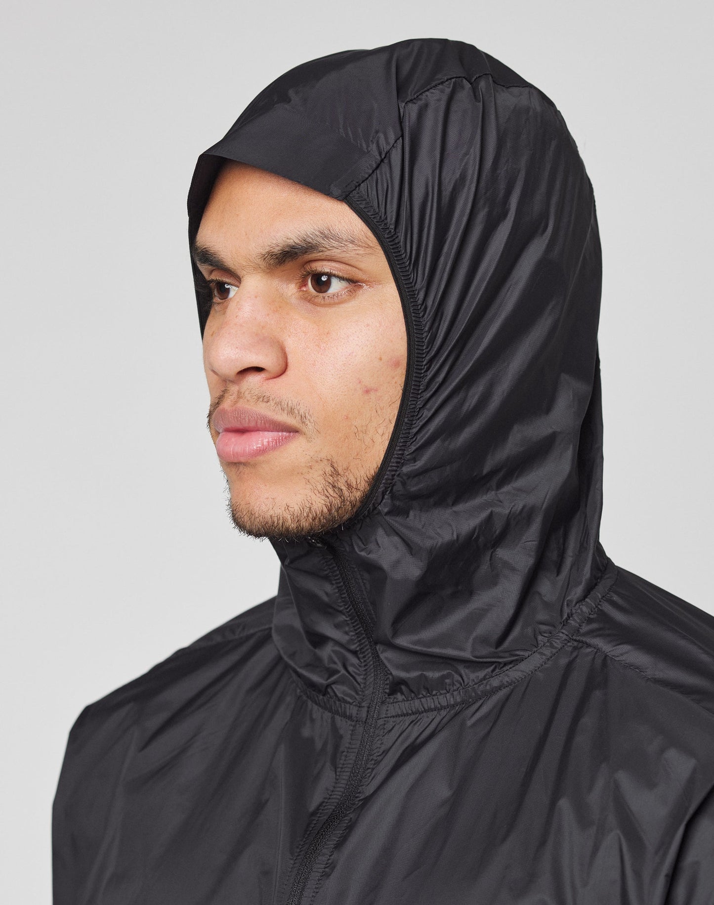 A person wears the LIVE FAST DIE YOUNG Live Fast Performance Running Jacket in black, regular fit with a visor hood up, looking left against a plain light gray background.