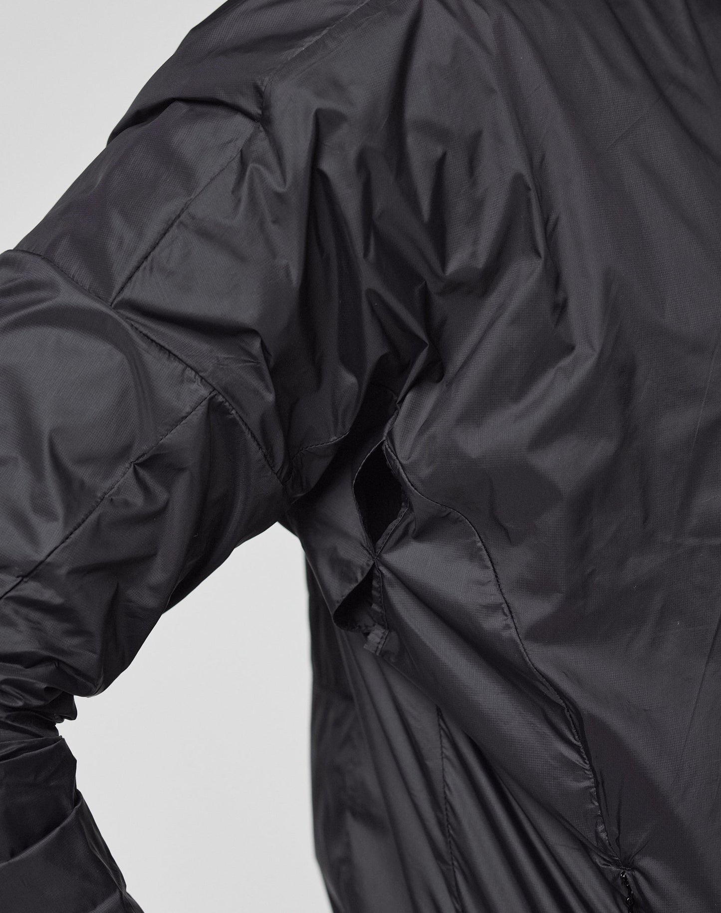 A close-up shows a person wearing the black, shiny Live Fast Performance Running Jacket by LIVE FAST DIE YOUNG. The Regular Fit jacket’s seams are visible on the arm and side, set against a plain light background.