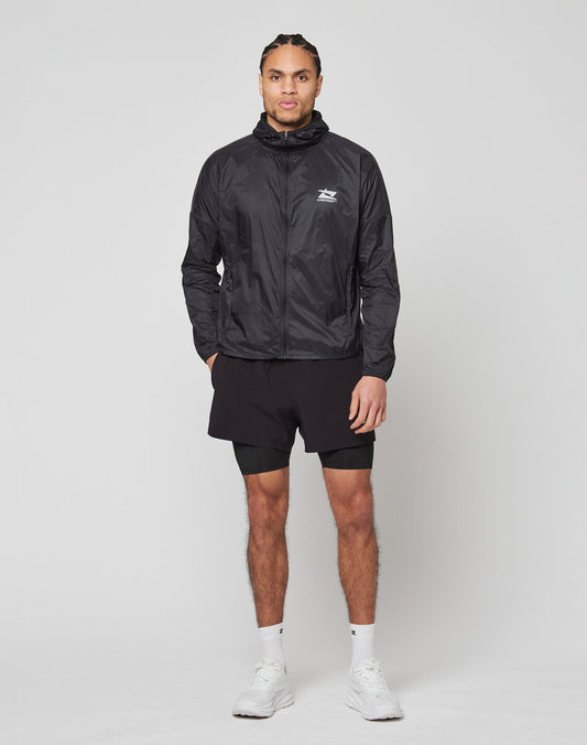 A man stands facing forward in a black LIVE FAST DIE YOUNG Live Fast Performance Running Jacket with reflective front print, black shorts, white ankle socks, and white sneakers against a plain light background.