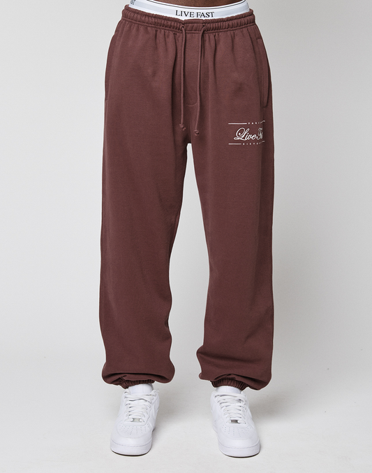 Someone wears maroon Wide Cuff Jogger by LIVE FAST DIE YOUNG, featuring "Live Fast" text on the left thigh and elastic waistband, paired with white sneakers against a plain backdrop.