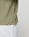 Close-up of a person wearing the olive-green LIVE FAST DIE YOUNG Basic Waffle Longsleeve in Oversize Fit with a small black flag label, paired with light grey pants against a plain, light background.