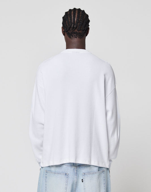 A person with braided hair wears the LIVE FAST DIE YOUNG Blank Waffle Longsleeve in oversize white (100% Baumwolle) and light blue jeans, standing with their back to the camera against a plain light gray background.