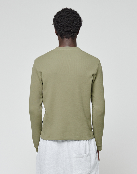 A person with short curly hair stands with their back to the camera, wearing a LIVE FAST DIE YOUNG Basic Waffle Longsleeve in olive green and light gray pants with a visible back pocket, set against a plain white background.