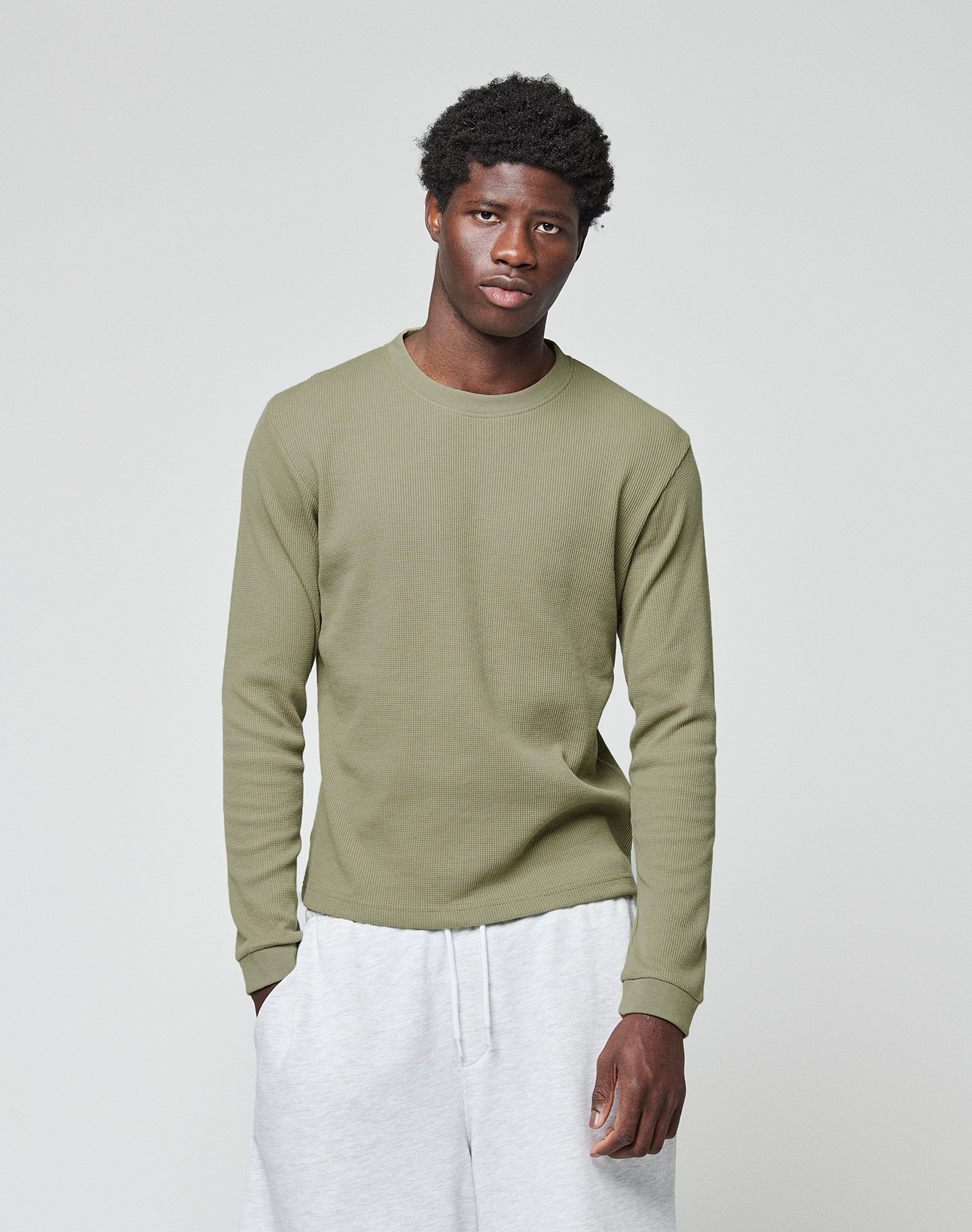 A man stands against a plain light background, wearing the LIVE FAST DIE YOUNG Basic Waffle Longsleeve in olive green and light gray sweatpants, looking directly at the camera with a neutral expression.