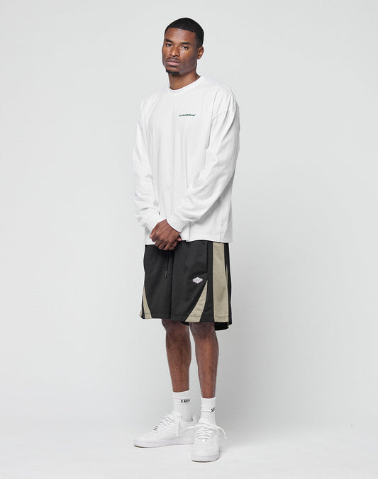 A man stands against a plain white background wearing a LIVE FAST DIE YOUNG Basic Longsleeve in white, black and beige athletic shorts, white crew socks, and white sneakers. His hands are clasped as he looks calmly at the camera.