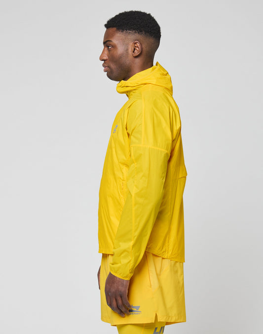 A man stands in profile against a plain background, wearing the LIVE FAST DIE YOUNG Live Fast Performance Running Jacket in bright yellow with Kapuze mit Visor and matching yellow shorts.