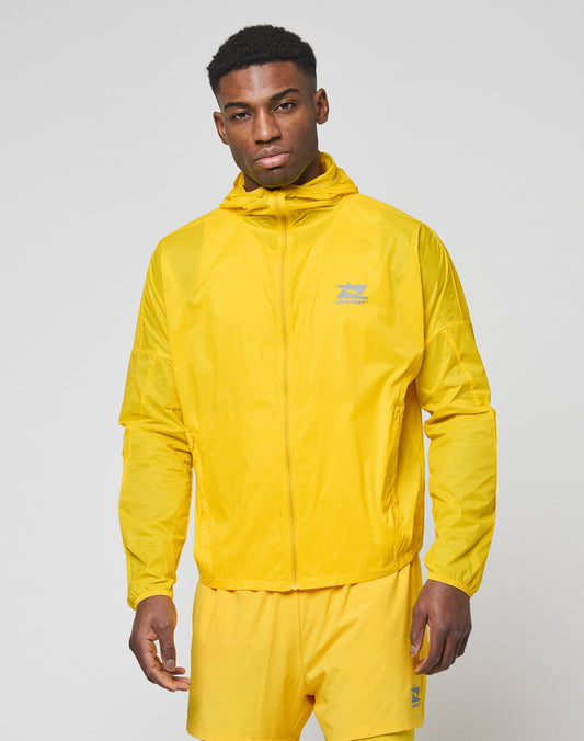 A man wearing the LIVE FAST DIE YOUNG Live Fast Performance Running Jacket in bright yellow with matching shorts stands against a plain light gray background, looking directly at the camera with a neutral expression.