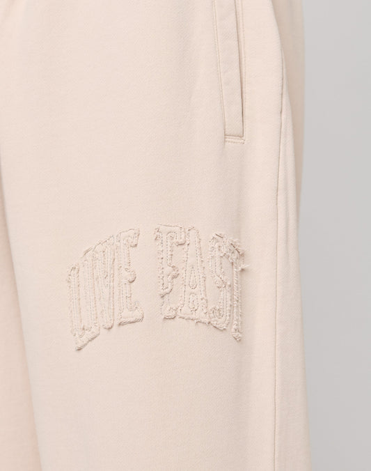 Close-up of Ripped College Wide Jogger by LIVE FAST DIE YOUNG in light beige, crafted from soft Baumwolle, with textured embroidered LIVE FAST text near the pocket.