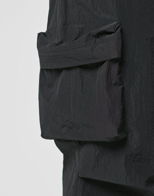 Close-up of textured black fabric with a large rectangular Cargotasche sewn on, part of LIVE FAST DIE YOUNG’s Live Fast Nylon Pants, shown against a plain light background.