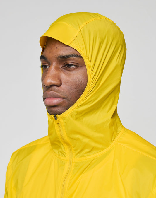 A person models the bright yellow Live Fast Performance Running Jacket by LIVE FAST DIE YOUNG, featuring a visor hood and Regular Fit, standing out against a plain light gray background.
