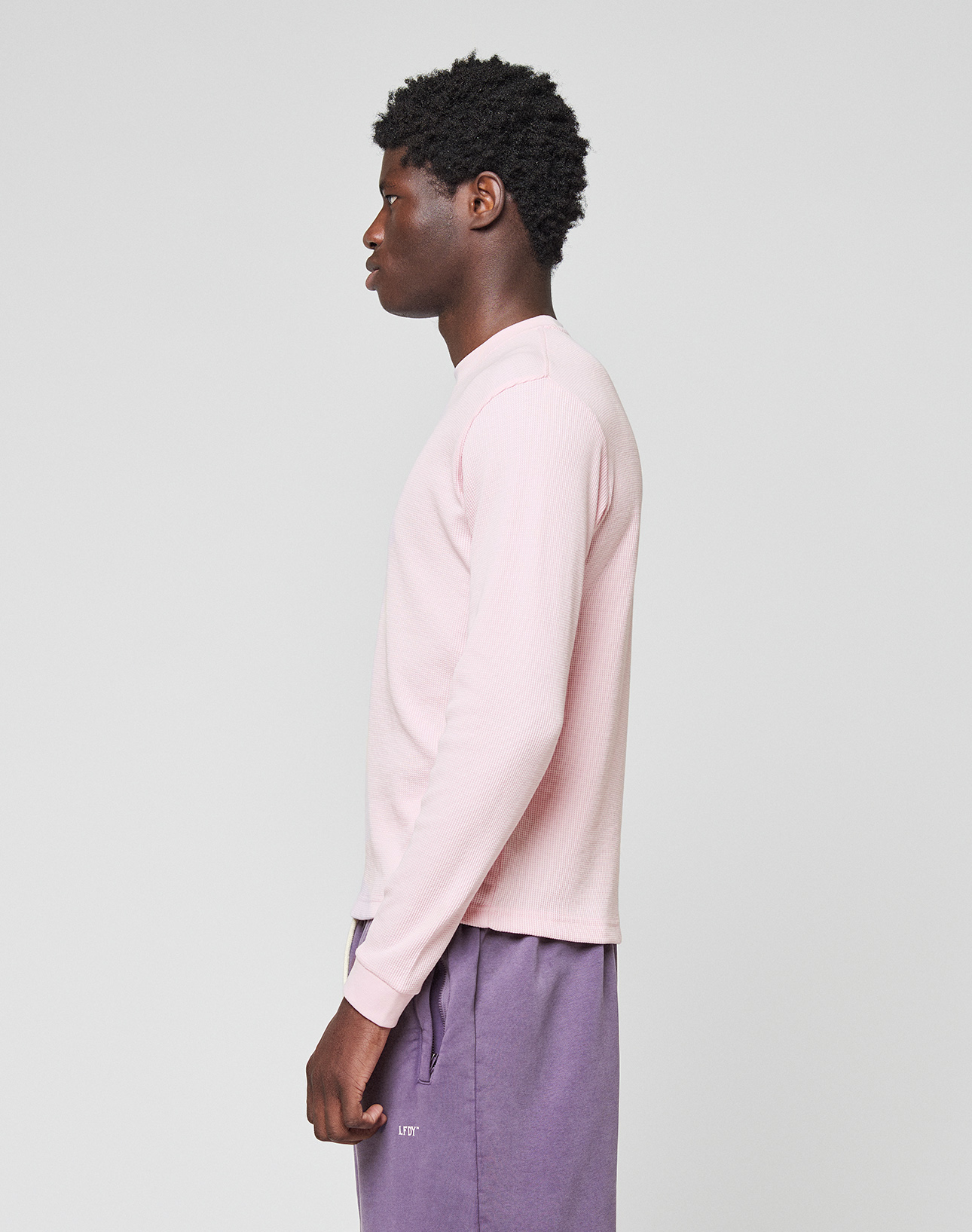 A person stands in profile against a plain background, wearing a Basic Waffle Longsleeve by LIVE FAST DIE YOUNG in light pink with Ripp-Bündchen and purple pants.