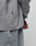 A close-up of a person wearing the LIVE FAST DIE YOUNG Basic Longsleeve and matching gray pants. The 100% Baumwolle shirt has an oversize fit and a small black tag on the side seam, with their hand partially visible.