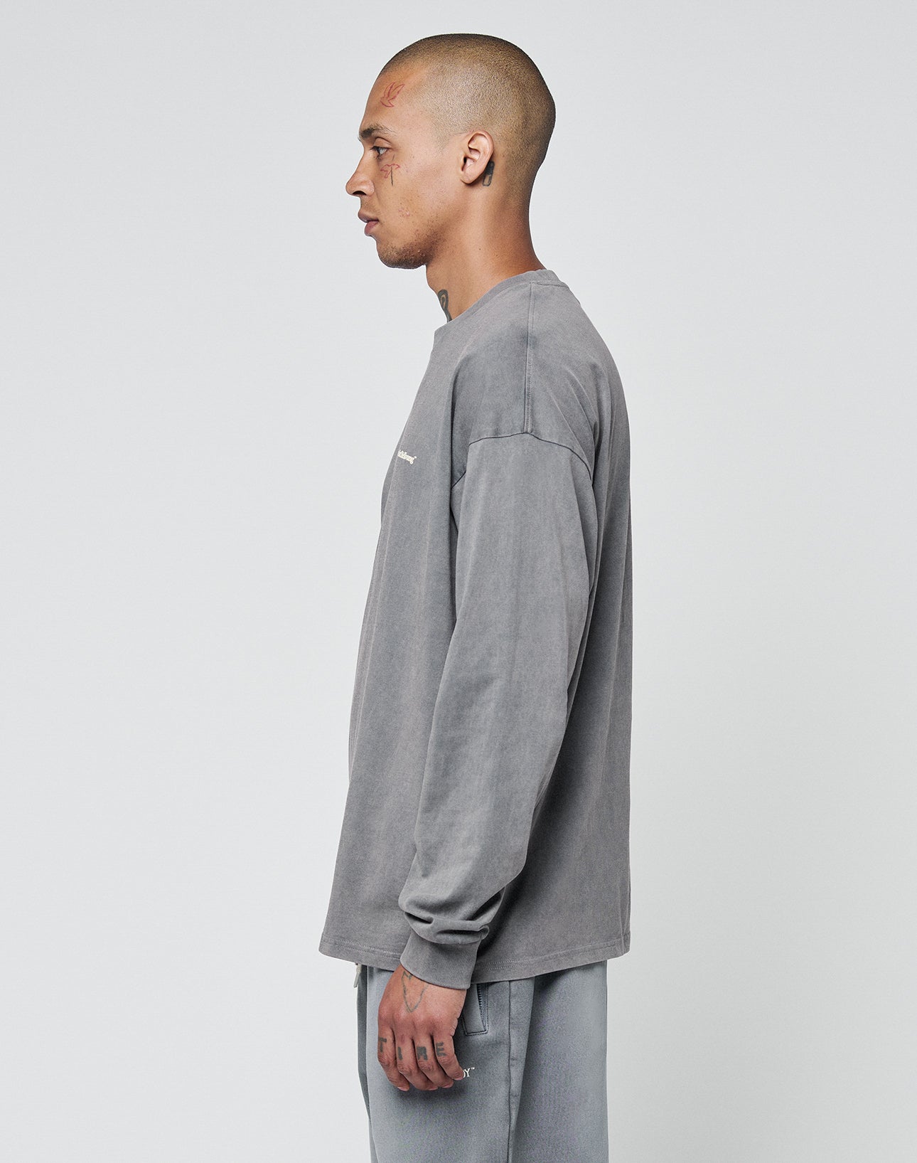 A man with a shaved head stands in profile against a plain background, wearing the LIVE FAST DIE YOUNG Basic Longsleeve and matching gray pants, both in an oversize fit and made from 100% Baumwolle.