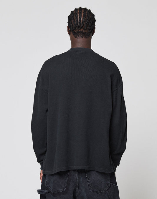 A person with short, braided hair faces away from the camera, wearing a LIVE FAST DIE YOUNG Blank Waffle Longsleeve in black and black pants with Ripp-Bündchen, set against a plain light gray background.