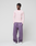 A person stands against a plain light background, wearing the LIVE FAST DIE YOUNG Basic Waffle Longsleeve in light pink, loose purple sweatpants with ribbed cuffs and white drawstring, and white sneakers, looking slightly to the side.
