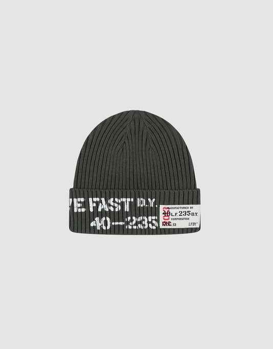 The Live Fast Army Beanie by LIVE FAST DIE YOUNG is a dark gray ribbed knit hat made from 100% Baumwolle, featuring white text and a small frayed web label with numbers and symbols on the folded brim, shown on a plain light gray background. 